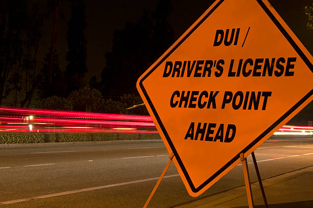 Orange DUI 'sobriety' and driver's license checkpoint ahead sign along side of road with car light trails in background